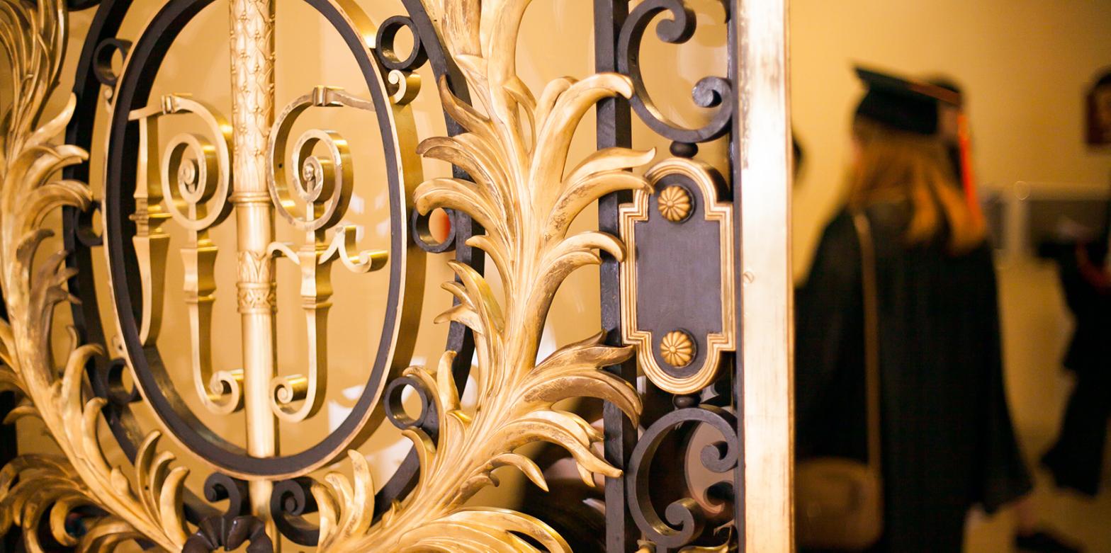 Porte dorée de la Sorbonne avec une diplômée en toge et son chapeau de dos au loin