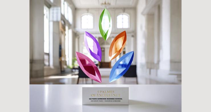 Trophée des 5 palmes de couleurs (bleu, orange, verte, violet, rose) Eduniversal derrière un fond blanc avec des colonnes