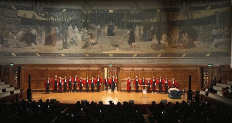 Photos de loin d'une dizaine de professeurs alignées face à la scène et au public en toge rouge avec la fresque du Grand Amhithéâtre de la Sorbonne derrière eux