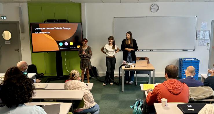 Amphithéâtre avec des élèves pris de dos et deux personnes qui présente sur un écran le Concours Jeunes Talents d'Orange. 