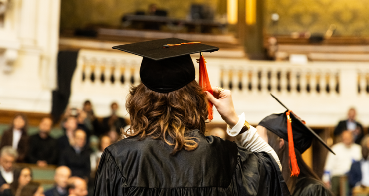 diplômée de dos qui tient son chapeau et vetue de sa toge dans le Grand Amphithéâtre de la Sorbonne