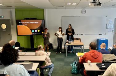 Amphithéâtre avec des élèves pris de dos et deux personnes qui présente sur un écran le Concours Jeunes Talents d'Orange. 