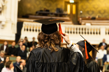 diplômée de dos qui tient son chapeau et vetue de sa toge dans le Grand Amphithéâtre de la Sorbonne