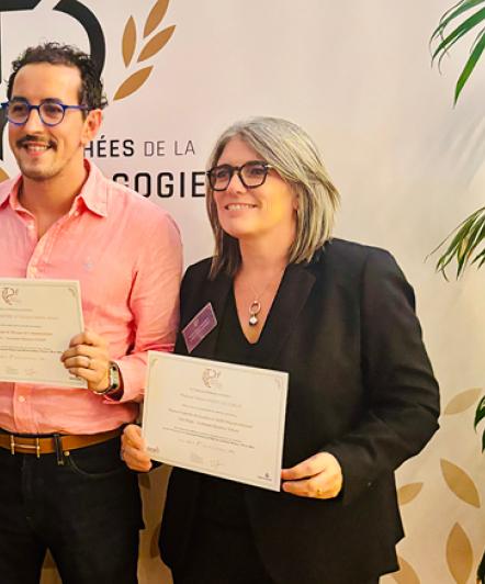 Deux femmes et au milieu un homme enseignant tenant des diplômes dans la main et sont phographiés debout sur le côté nous voyons le logo du Trophée de la pédagogie