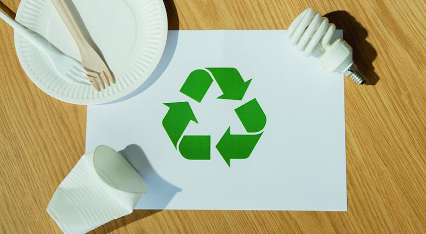 Logo vers de tri sur une feuille posée sur une table accompagnée d'une ampoule, un assiette en carton et des couverts puis un gobelet
