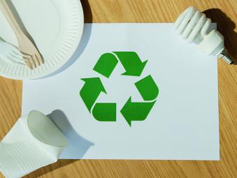 Logo vers de tri sur une feuille posée sur une table accompagnée d'une ampoule, un assiette en carton et des couverts puis un gobelet