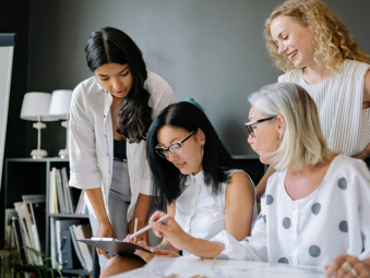4 filles autour d'un ipad qui travaille ensemble dans la bonne humeur