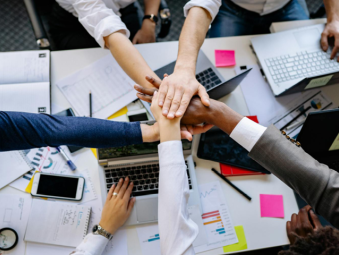 Plusieurs mains se joignent au-dessus d'une table pour montrer l'esprit d'équipe