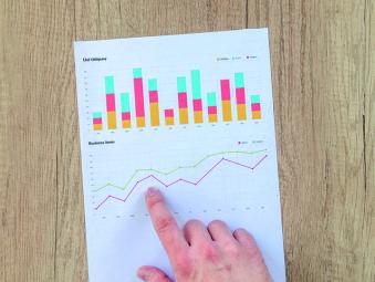 Doigt qui pointe une infographie avec des graphiques sur une table en bois