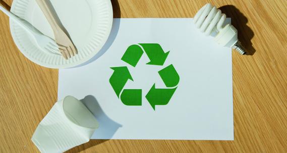 Logo vers de tri sur une feuille posée sur une table accompagnée d'une ampoule, un assiette en carton et des couverts puis un gobelet