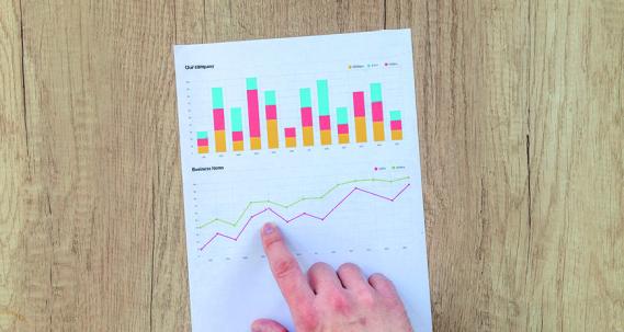 Doigt qui pointe une infographie avec des graphiques sur une table en bois